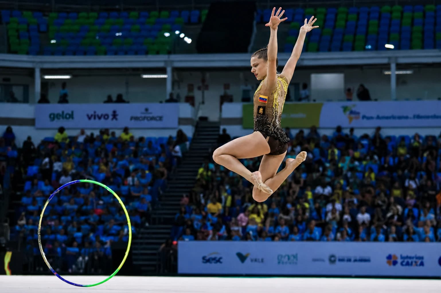 Rhythmic gymnast performing a split leap through a hoop on a competition floor